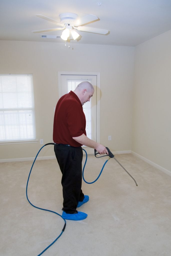 Man using a cleaning tool in an empty room, wearing protective shoe covers, illustrating professional cleaning services for residential properties.