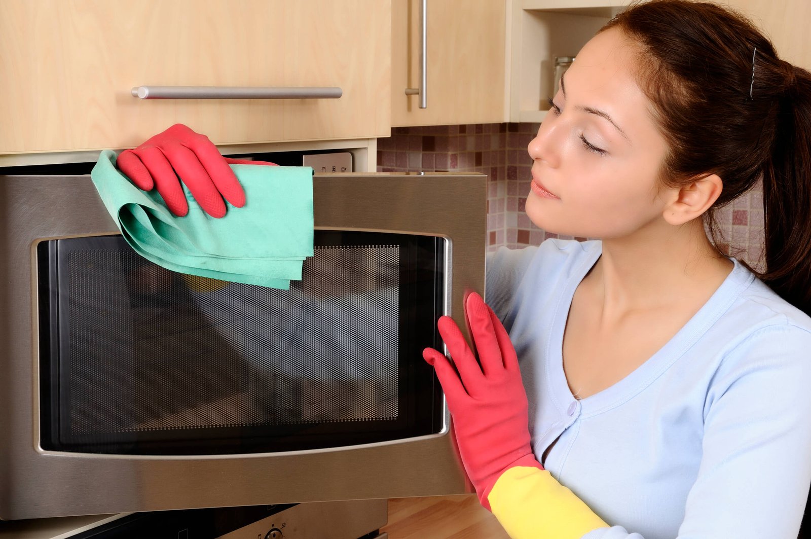Woman in gloves cleaning a microwave with a cloth, emphasizing home cleanliness and professional cleaning services in Melbourne.
