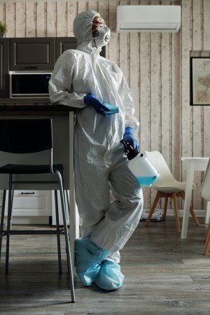 Professional in protective gear standing in a clean kitchen, holding a disinfectant spray bottle, emphasizing residential disinfection services to combat harmful bacteria and viruses.