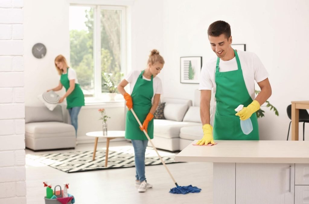 Professional cleaners in green aprons performing house cleaning tasks in a bright, modern living room, highlighting GSR Cleaning's commitment to high-quality and reliable cleaning services in Richmond.